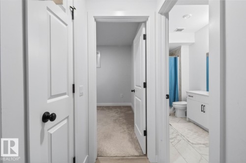 White paneled doors with black hardware, neutral carpeted room, and a bathroom featuring a white vanity with black pulls and white tile flooring - 4023 Hawthorn Link Link Sw, Edmonton, AB 