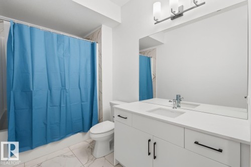 Contemporary bathroom featuring a white vanity with integrated sink, rectangular mirror, and a three-light fixture - 4023 Hawthorn Link Link Sw, Edmonton, AB 