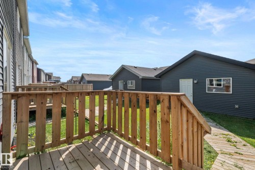 Wood deck with railings and a wooden walkway leading to a dark-sided structure with a white door and window - 4023 Hawthorn Link Link Sw, Edmonton, AB 