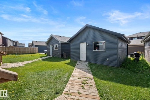 Expansive backyard featuring a manicured lawn, wooden walkways, and an outbuilding with a white door and window - 4023 Hawthorn Link Link Sw, Edmonton, AB 