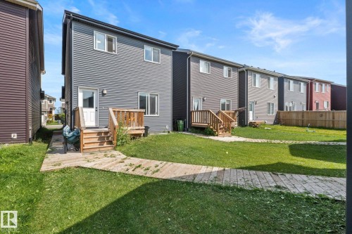 Rear exterior featuring gray horizontal siding, an elevated wood deck with stairs, a white door, and multiple windows - 4023 Hawthorn Link Link Sw, Edmonton, AB 