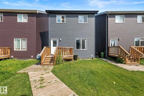 Two-story exterior with horizontal siding, multiple windows, and a rear door opening onto a wood-finish deck with stairs - 4023 Hawthorn Link Link Sw, Edmonton, AB 