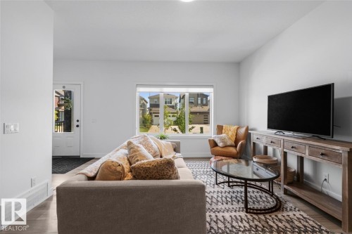 Light-filled living area featuring wood-finish flooring and a white entry door with glass paneling - 4023 Hawthorn Link Link Sw, Edmonton, AB 