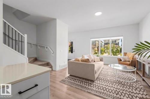 Integrated living area with wood-finish flooring, a large picture window, and a staircase featuring black metal spindles - 4023 Hawthorn Link Link Sw, Edmonton, AB 
