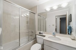 Bathroom featuring a tub/shower combination with sliding glass doors, a vanity with an undermount sink, a large mirror, and overhead lighting - 