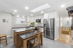 Kitchen featuring white cabinetry, stainless steel appliances, a center island with seating, a skylight, and tile flooring - 
