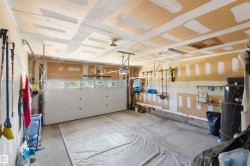 Spacious garage featuring a white overhead door with upper window panels, concrete flooring, and an accessible attic hatch - 