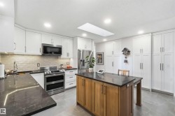 Modern kitchen featuring white cabinetry with ample storage, stainless steel appliances, dark countertops, and a wood-finish island - 