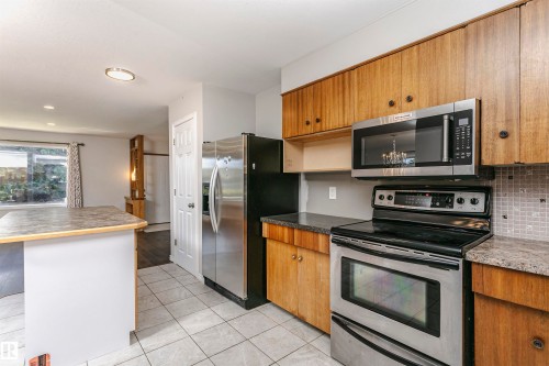 Kitchen featuring wood cabinetry, stainless steel appliances, tile flooring, and a breakfast bar - 11440 44A Avenue Nw, Edmonton, AB 