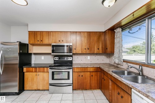 U-shaped kitchen featuring wood-finish cabinetry, stainless steel appliances, a double basin sink, and tile flooring - 11440 44A Avenue Nw, Edmonton, AB 