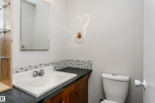 Vanity with a built-in sink, wood-finish cabinetry, dark countertop, and tiled backsplash - 11440 44A Avenue Nw, Edmonton, AB 