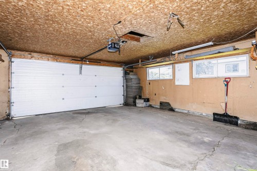 Spacious garage with concrete flooring, overhead door with modern hardware, and exposed beam ceiling - 11440 44A Avenue Nw, Edmonton, AB 
