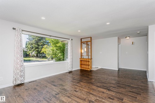 Spacious room featuring wood-finish flooring, recessed lighting, a large picture window, and a built-in wooden room divider with integrated pendant lighting - 11440 44A Avenue Nw, Edmonton, AB 