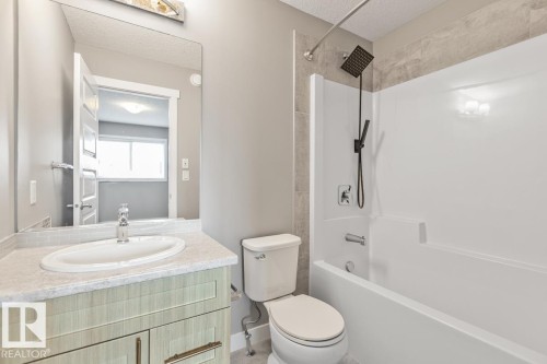 Full bathroom featuring a single vanity with an integrated sink, a tiled backsplash, and a tub with a shower head and hand shower - 22 Hope Common, Spruce Grove, AB 