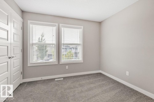 Neutral wall tones with crisp white trim, two windows with blinds, plush gray carpeting, and a paneled interior door - 22 Hope Common, Spruce Grove, AB 