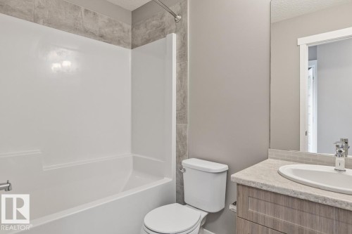Tub/shower combination with tile surround, wood-finish vanity with countertop, undermount sink, and large mirror - 22 Hope Common, Spruce Grove, AB 