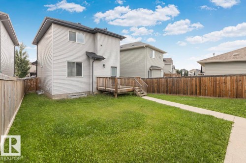 Spacious backyard featuring a wooden privacy fence, a concrete walkway, and a raised wooden deck with stairs - 22 Hope Common, Spruce Grove, AB 