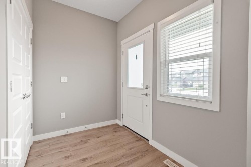 Entryway featuring a vaulted ceiling, wood-finish flooring, white paneled doors, and a window with blinds - 22 Hope Common, Spruce Grove, AB 