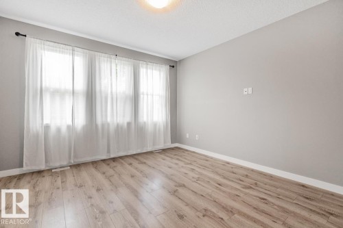 Three large windows providing ample natural light, wood-finish flooring, white baseboards, and a neutral wall color - 22 Hope Common, Spruce Grove, AB 