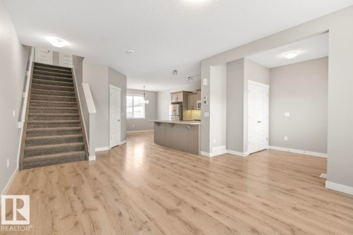 Wood-finish flooring throughout, carpeted staircase, recessed lighting, white trim, and a kitchen featuring wood-finish cabinetry - 22 Hope Common, Spruce Grove, AB 