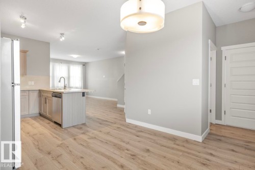 Wood-finish flooring throughout, kitchen island with integrated sink, stainless steel dishwasher, light-toned cabinetry, and recessed lighting - 22 Hope Common, Spruce Grove, AB 