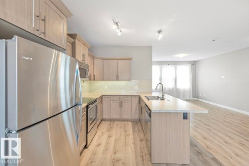 Kitchen featuring stainless steel appliances, wood-finish flooring, light-toned cabinetry, light-toned countertops, and a double basin sink - 22 Hope Common, Spruce Grove, AB 