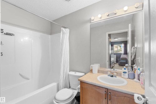 White tub/shower combination, built-in vanity with single basin sink, wood-finish cabinetry, and overhead vanity lighting - 13028 34 Street Nw, Edmonton, AB 