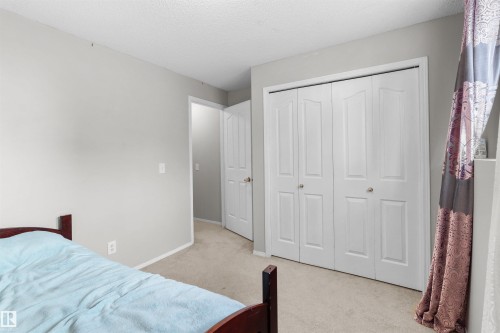 Neutral paint palette, textured carpet, white bi-fold closet doors, white paneled interior door, and textured ceiling - 13028 34 Street Nw, Edmonton, AB 