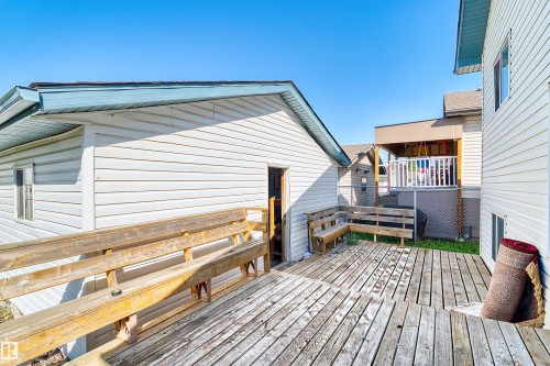 Expansive wood deck with built-in benches, white vinyl siding exterior, and a secondary covered deck structure - 13028 34 Street Nw, Edmonton, AB 