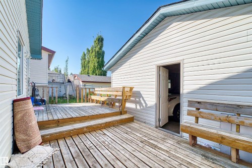 Expansive wood deck with stairs, featuring a detached garage with vinyl siding and a side entry door - 13028 34 Street Nw, Edmonton, AB 