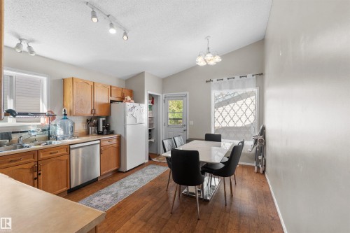 Vaulted ceilings, wood-finish flooring, stainless steel dishwasher, track lighting, and a white paneled door - 13028 34 Street Nw, Edmonton, AB 