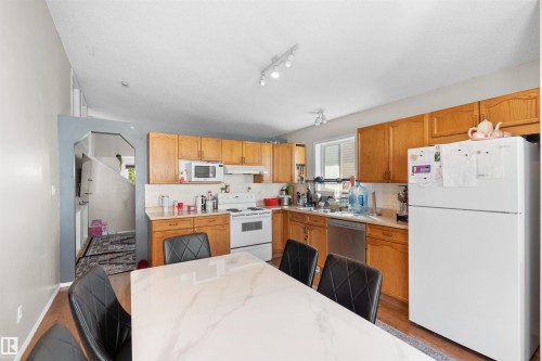 Kitchen featuring wood-finish cabinetry, white appliances, track lighting, and a window - 13028 34 Street Nw, Edmonton, AB 