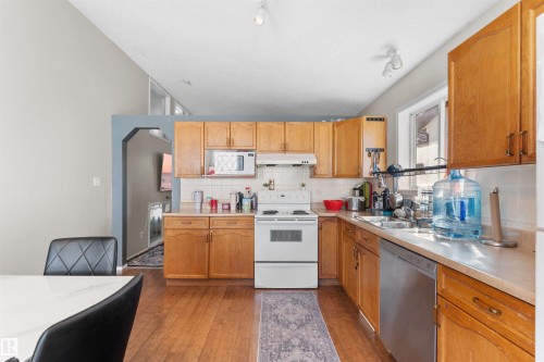 Kitchen featuring wood-finish cabinetry, stainless steel dishwasher, white range, and a vaulted ceiling - 13028 34 Street Nw, Edmonton, AB 
