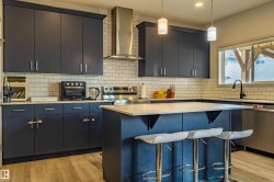 Kitchen featuring dark blue cabinetry, light subway tile backsplash, white countertops, and wood-finish flooring - 