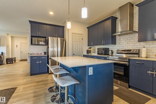 Modern kitchen featuring blue cabinetry, stainless steel appliances, a white subway tile backsplash, and light wood-finish flooring - 41 Sequoia Bend, Fort Saskatchewan, AB 