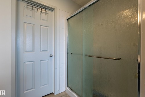 Shower enclosure featuring a framed frosted glass door with chrome hardware, complemented by a white paneled door with a spherical chrome knob - 41 Sequoia Bend, Fort Saskatchewan, AB 