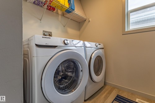 Dedicated laundry area featuring a front-load washer and dryer set, wire shelving, a window, and wood-finish flooring - 41 Sequoia Bend, Fort Saskatchewan, AB 