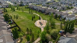 Expansive green space featuring a circular playground area, paved walking paths, and numerous mature trees - 