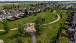 Expansive green space featuring a winding paved pathway, mature trees, a sand-based playground area, and surrounding residential properties - 