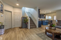 Open-concept main level featuring wood-finish flooring, a carpeted staircase with white railings, a kitchen island with pendant lighting, and white subway tile backsplash - 