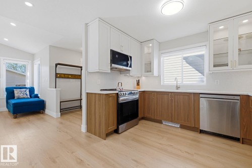 Modern kitchen featuring stainless steel appliances, two-tone cabinetry, light countertops, and wood-finish flooring - 3830 22 Street Nw, Edmonton, AB 