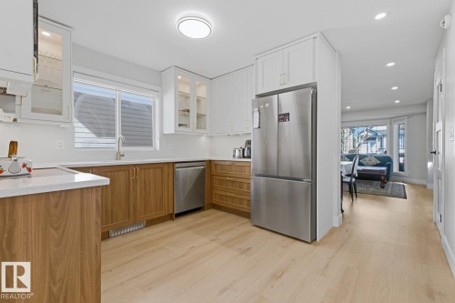 Modern kitchen featuring stainless steel appliances, wood-finish flooring, white upper cabinetry, and wood-finish lower cabinetry - 3830 22 Street Nw, Edmonton, AB 