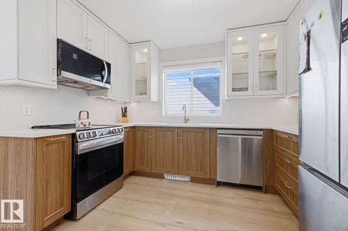 Contemporary kitchen featuring two-tone cabinetry, stainless steel appliances, wood-finish flooring, and a white backsplash - 3830 22 Street Nw, Edmonton, AB 