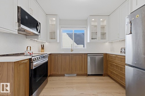 U-shaped kitchen featuring wood-finish base cabinetry, white upper cabinetry with glass-front accents, and stainless steel appliances - 3830 22 Street Nw, Edmonton, AB 