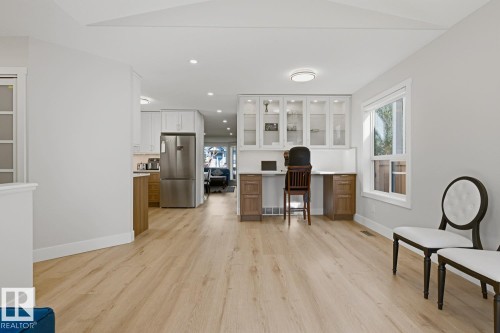 Light wood-finish flooring throughout, integrated desk area with built-in cabinetry, stainless steel refrigerator, and ample natural light from exterior windows - 3830 22 Street Nw, Edmonton, AB 
