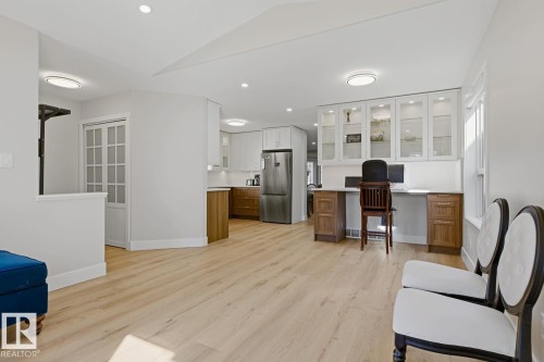 Light wood-finish flooring throughout, recessed lighting, built-in desk with overhead glass-front cabinetry, stainless steel refrigerator, and white French doors - 3830 22 Street Nw, Edmonton, AB 