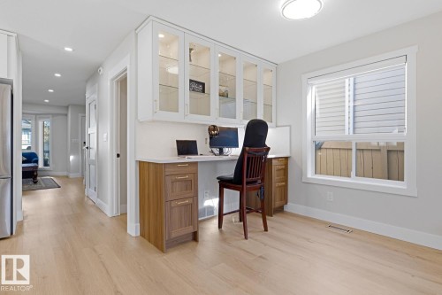 Built-in desk area with glass-front upper cabinetry and wood-finish lower cabinetry, light wood-finish flooring, recessed lighting, and a white-framed window - 3830 22 Street Nw, Edmonton, AB 
