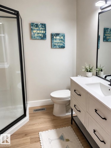 Spacious bathroom featuring a glass-enclosed shower, wood-finish flooring, a contemporary vanity with an integrated sink, and a wall-mounted mirror - 3830 22 Street Nw, Edmonton, AB 