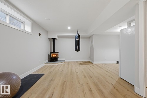 Recessed lighting, light wood-finish flooring, wood-burning stove with stone hearth, window, and white walls - 3830 22 Street Nw, Edmonton, AB 