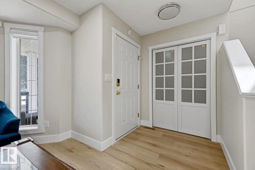 Wood-finish flooring with white baseboards, a solid white entry door, and white bi-fold doors with frosted glass panels - 3830 22 Street Nw, Edmonton, AB 